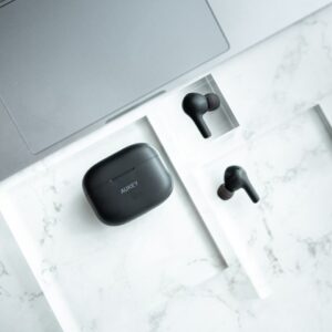 Top view of sleek wireless earbuds and case on a marble surface next to a laptop.