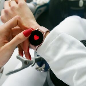 Close-up of a woman's hand with red nails interacting with a smartwatch displaying a heart icon.